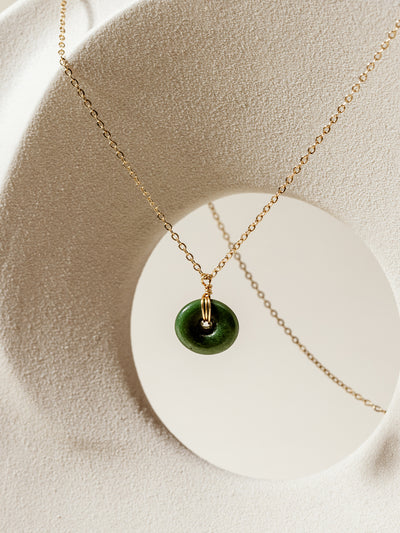 Gold chain necklace featuring a circular green glass pendant, elegantly displayed on a textured white modern sculpture, highlighting handcrafted and sustainable jewelry design.