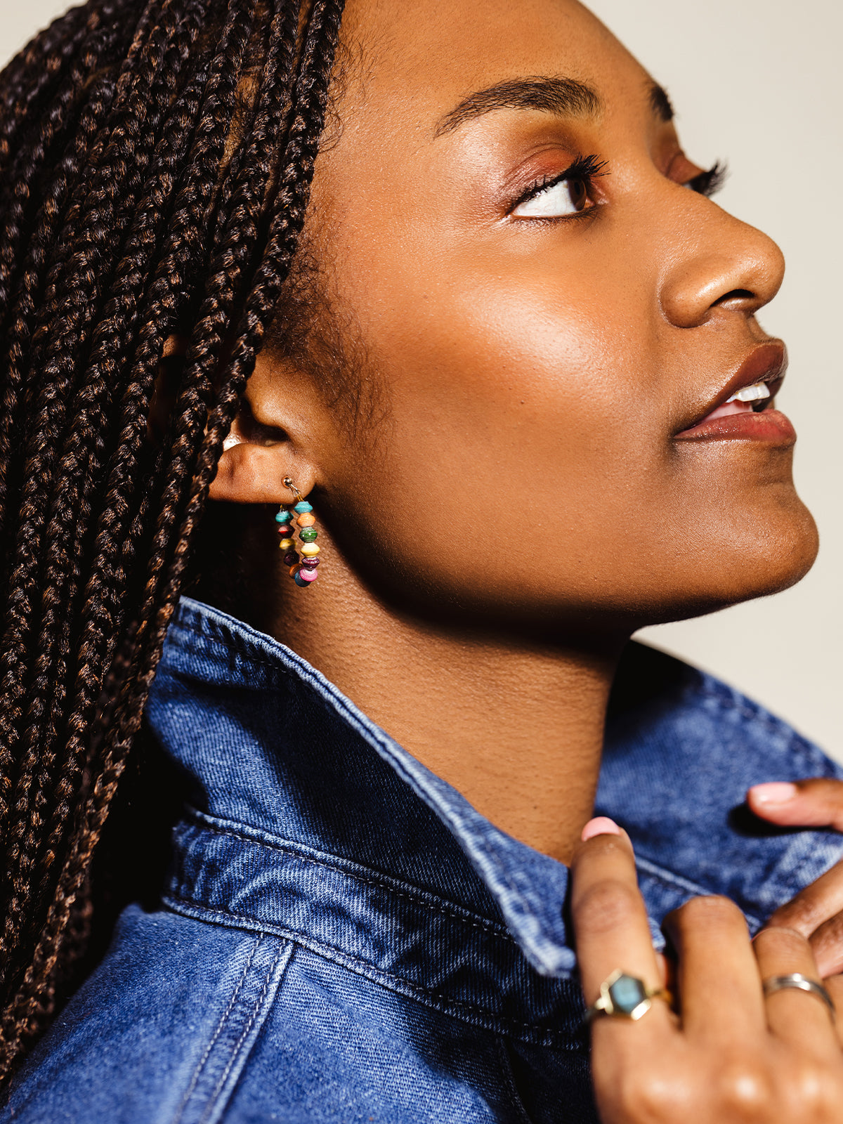 Close-up profile of a woman wearing colorful beaded hoop earrings paired with a denim jacket, showcasing a bold and sustainable fashion statement with handcrafted jewelry.