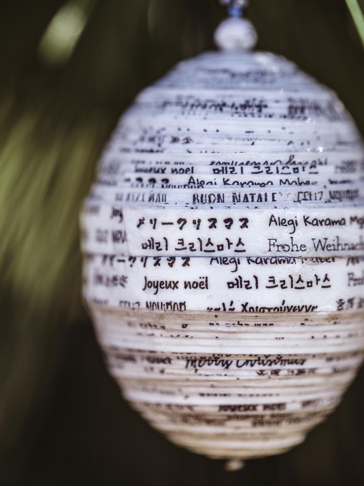 Close-up of a white handcrafted paper ornament with 'Merry Christmas' written in various languages, highlighting the intricate detailing and multilingual design.