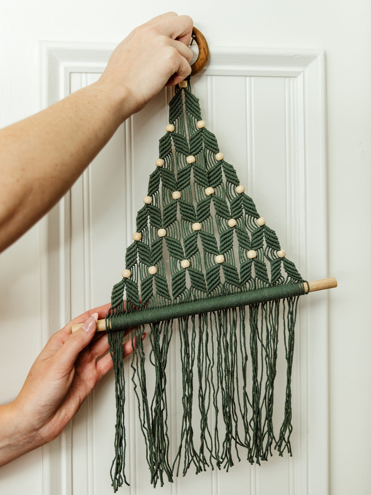 Green macrame Christmas
 tree wall hanging with beads. Wall hanging on white wall. 