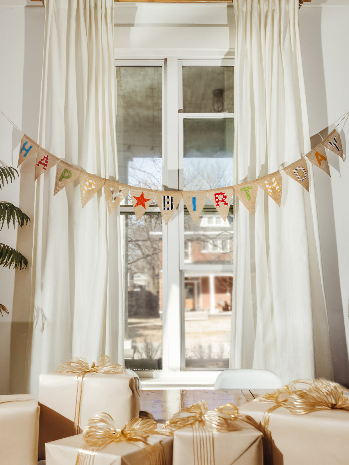 Handmade burlap birthday banner paired with neatly wrapped kraft paper gifts tied with golden ribbons, creating a warm and festive celebration setup.