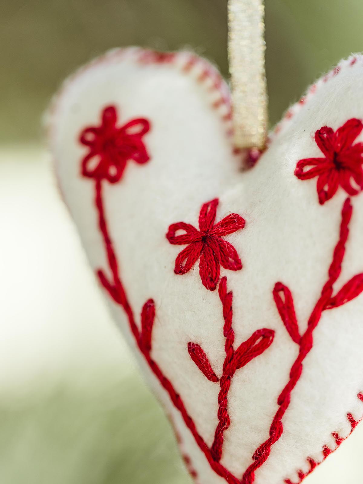 Close-up view of a handmade felt heart ornament with red embroidered flowers and detailed stitching, highlighting the intricate craftsmanship and festive design.