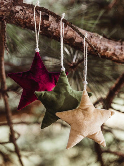 Handmade fabric star ornaments in burgundy, green, and beige, hanging from a pine tree branch with twine, adding a cozy and rustic touch to holiday decor.