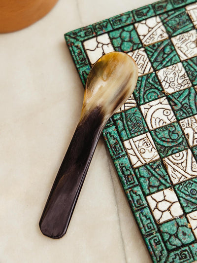 Short horn spoon on jade and white checker board on white counter top.