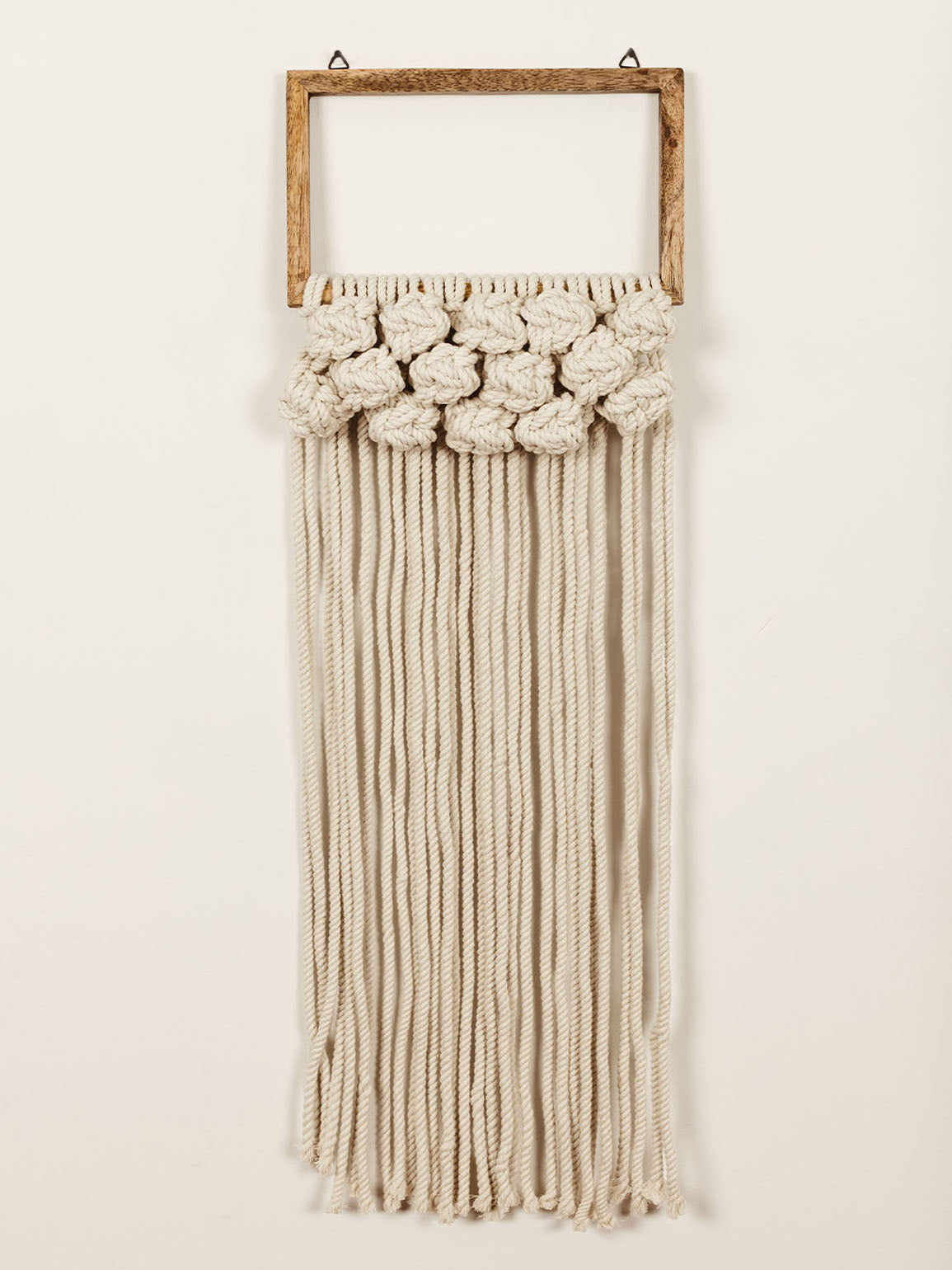 Rope wall hanging over white wall with square wooden top that has wall hanging hardware. 