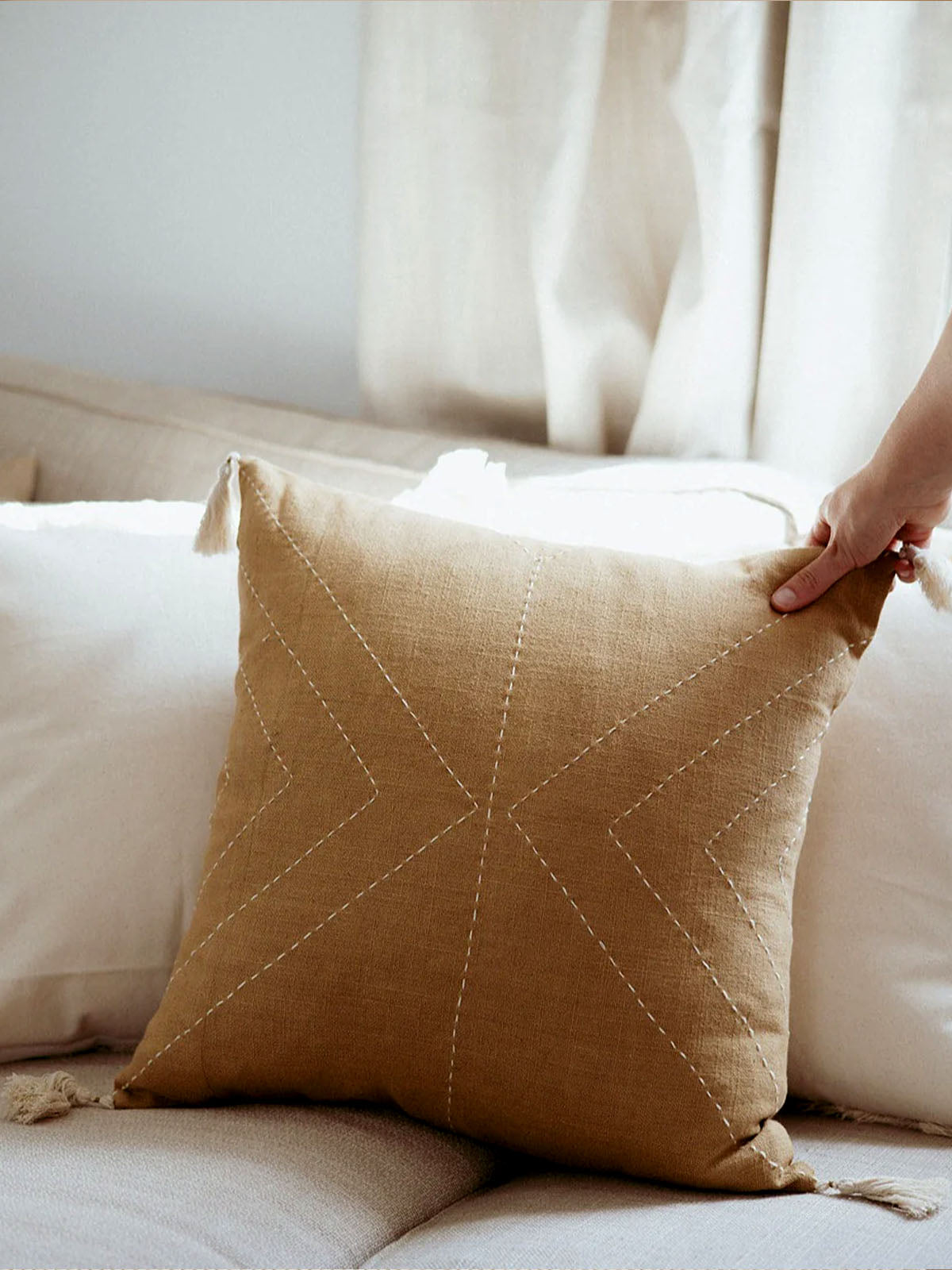 Mustard yellow pillow cover on cream couch with hand holding edge of pillow. 