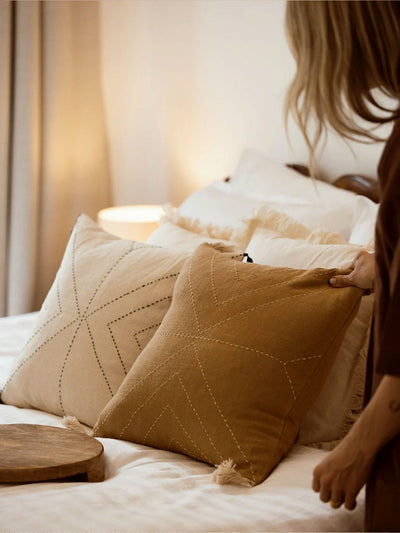 Mustard yellow pillow cover on cream bedding with hand holding edge of pillow. 