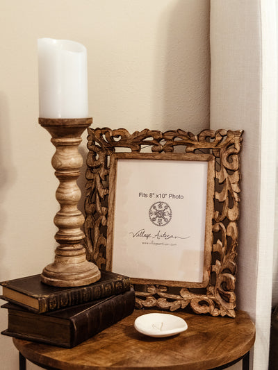 Village Artisan 8x10 carved wooden photo frame on a rustic side table with a vintage candle holder, books, and a trinket dish. Handcrafted home accessories from Joffa.