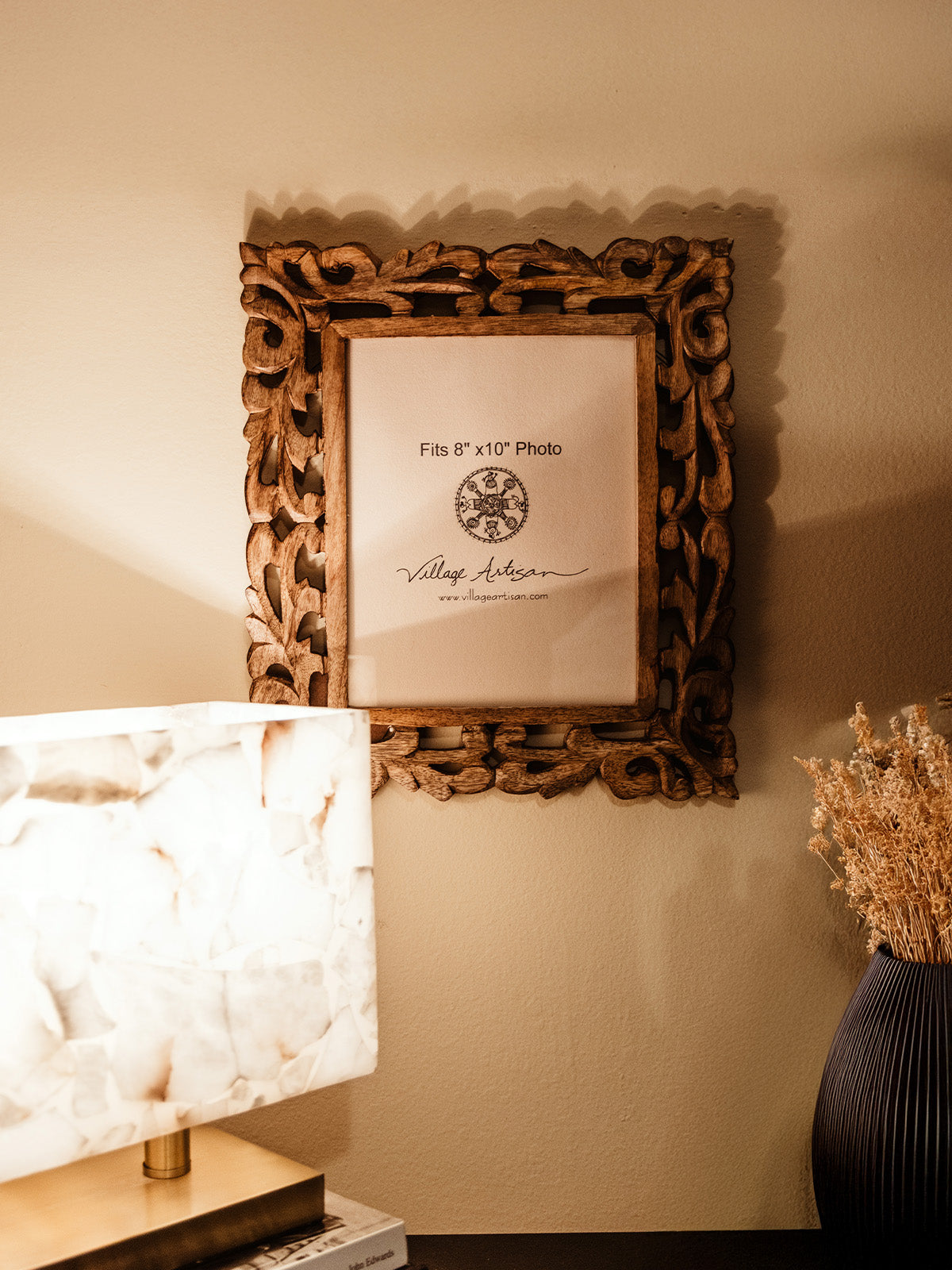 Village Artisan 8x10 carved wooden photo frame displayed on a side table with a modern marble lamp and dried floral arrangement. Ethically sourced home decor from Joffa.