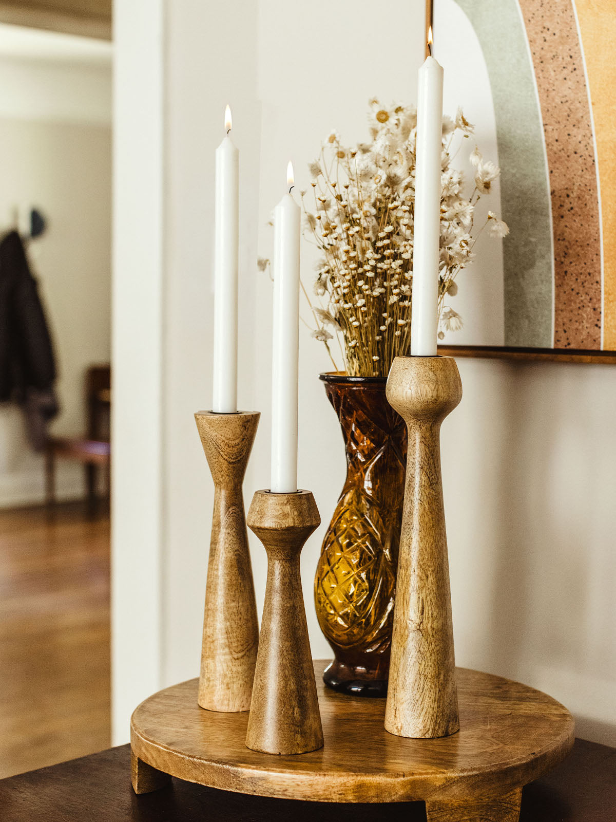 Wooden candle stand set on mango wood tray in living room space with some decor surrounding.