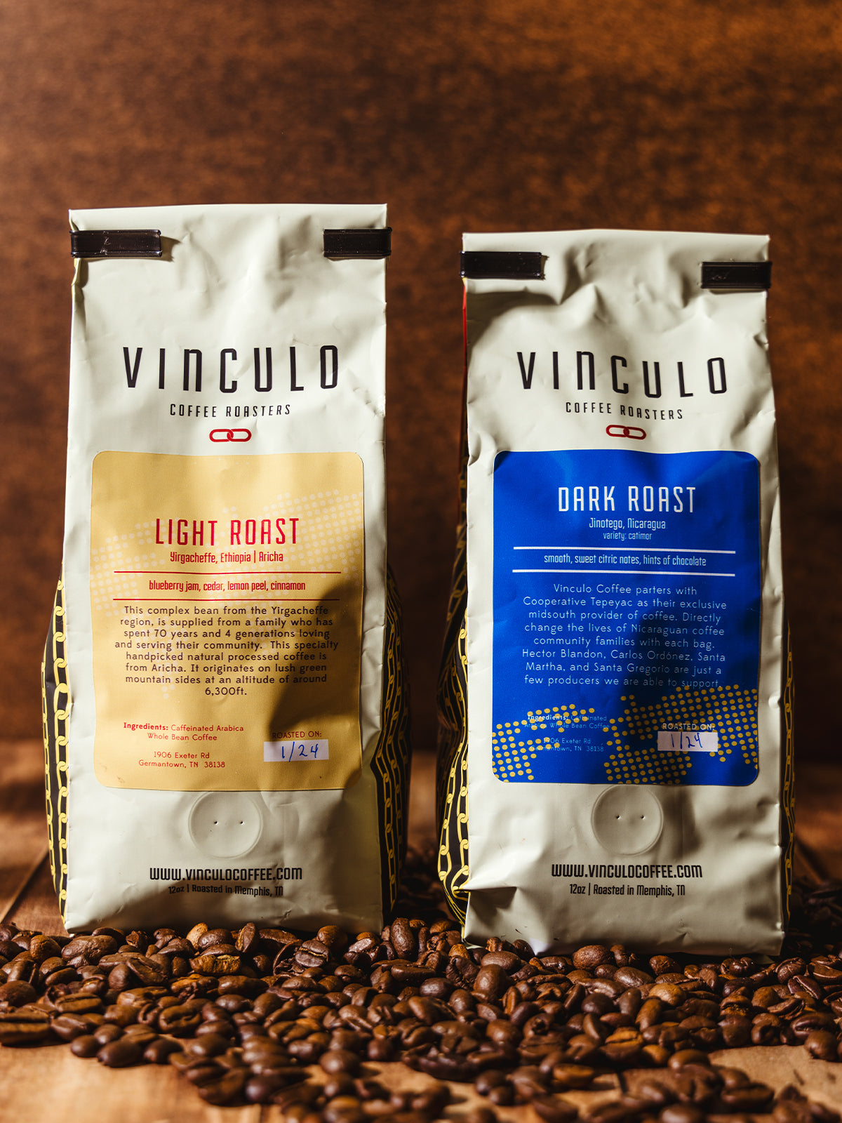 A front-facing view of two Vinculo Coffee Roasters bags, one Light Roast (yellow label) and one Dark Roast (blue label), placed on a rustic wooden surface with coffee beans scattered around. The warm lighting emphasizes the texture of the beans and the branding.