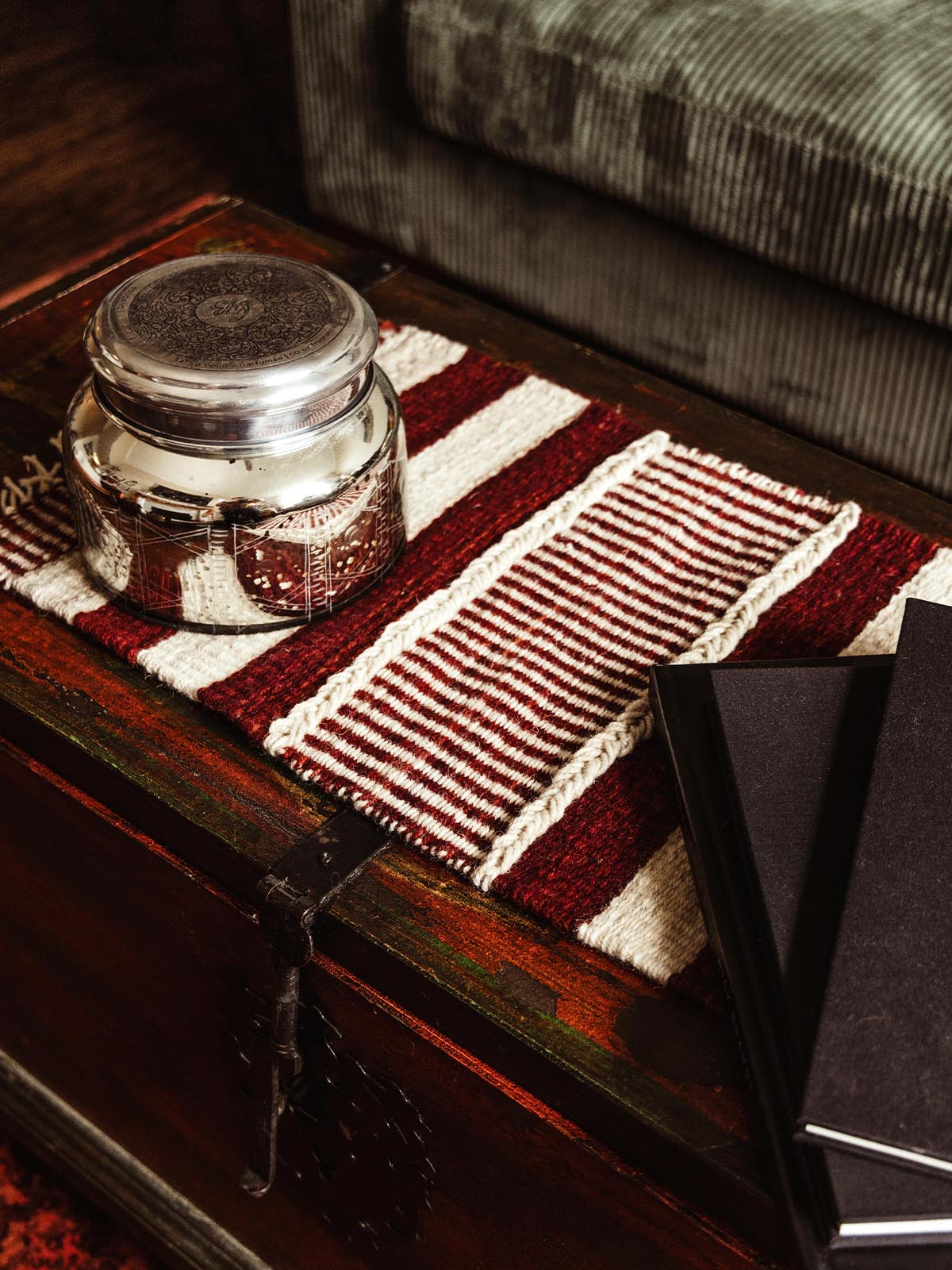 Decorative silver jar on a woven red and white striped table runner on a wooden chest. Handmade table decor adds a touch of warmth and charm to home interiors.