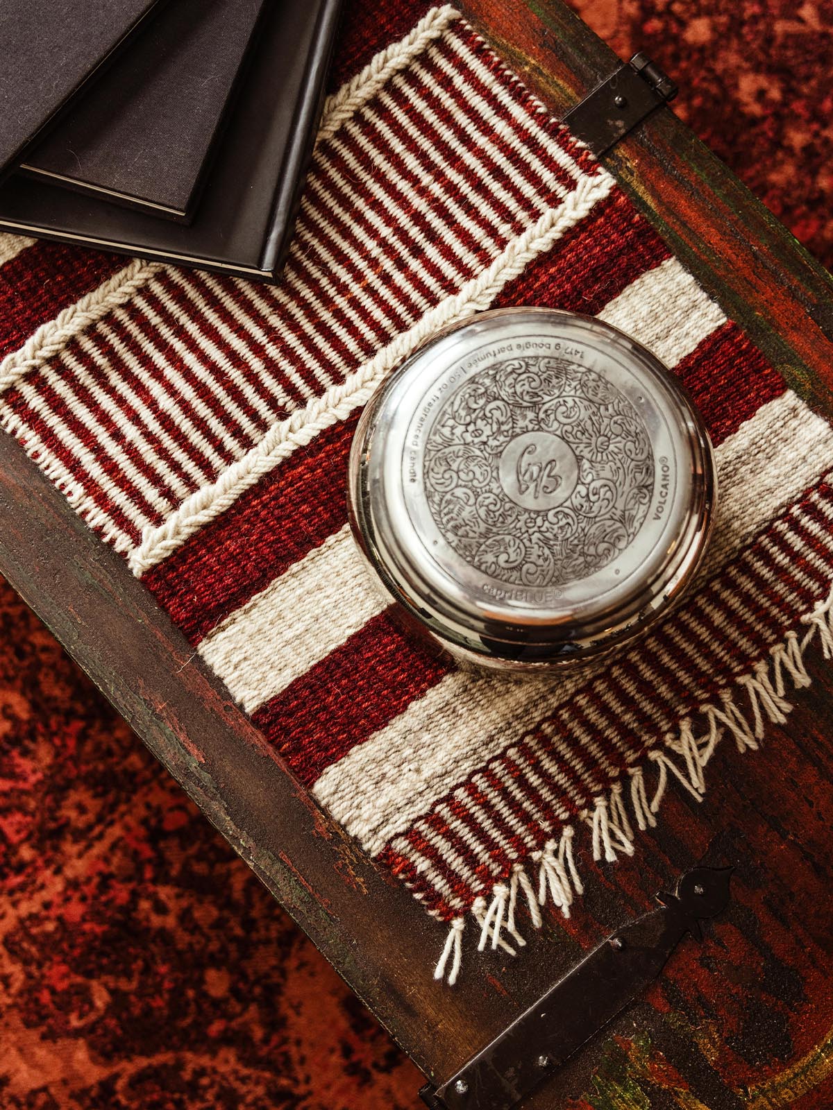 Top view of a silver jar and black notebooks placed on a red and white woven table runner. Rustic home decor with handcrafted details, perfect for cozy living spaces.