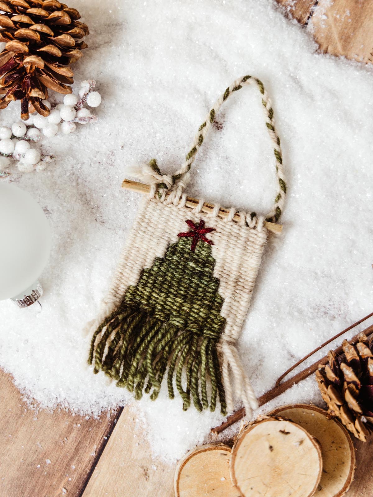 Small woven tree ornament surrounded by pinecones and faux snow, creating a winter holiday scene. Handcrafted holiday decor for adding rustic charm to the festive season.