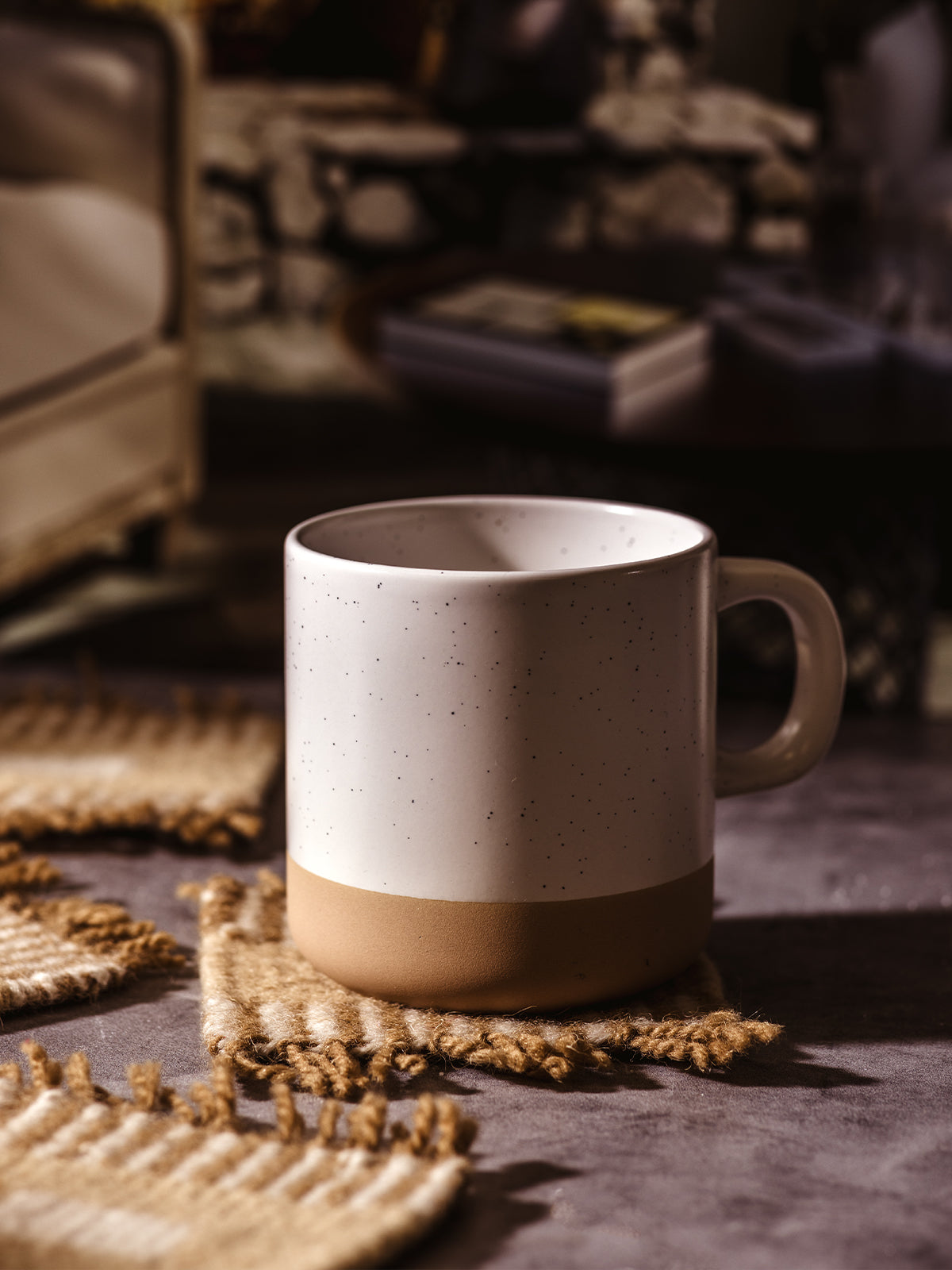 Speckled ceramic mug resting on a handwoven coaster, highlighting the warm textures of the woven material.