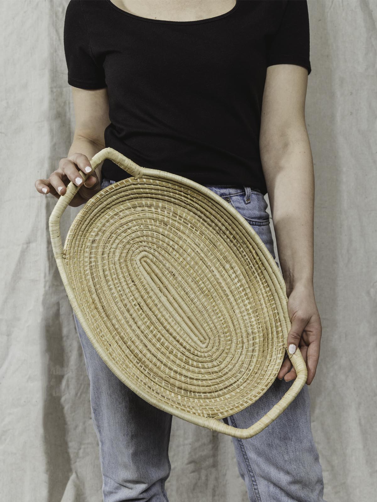 model holding large woven serving tray in a light tan color