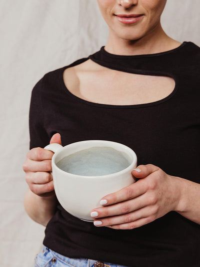 Model holding large off white soup mug with steel blue tones in the inside.